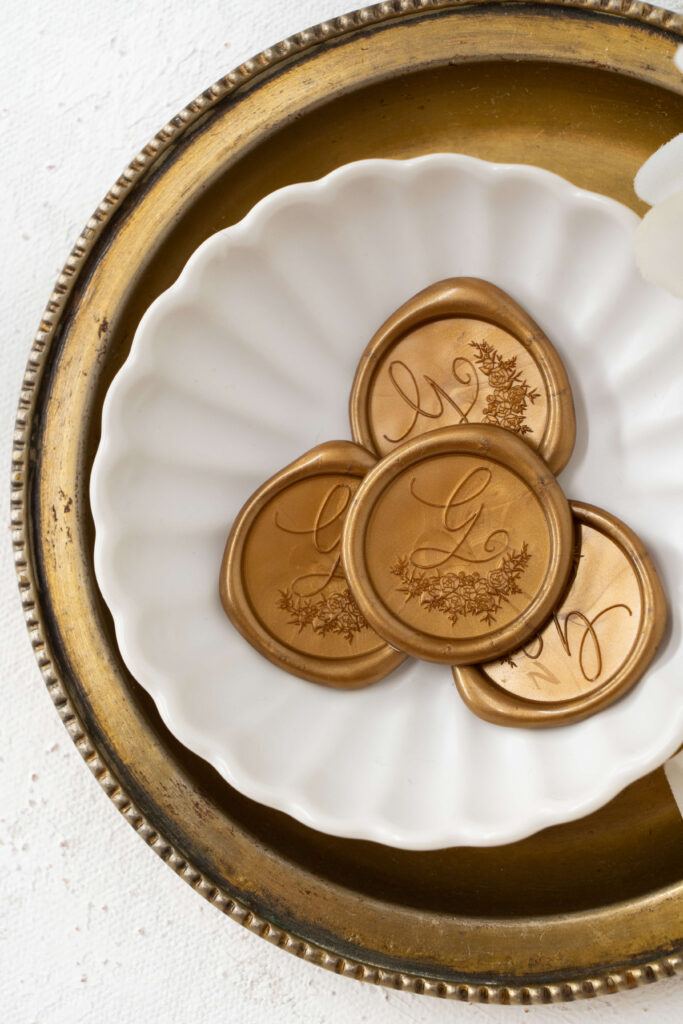 A brass dish holds a smaller dish filled with gold custom wax seals featuring the crest created specially for Mallory's wedding day. E Stokes Creations created round wax seals custom for her wedding day.