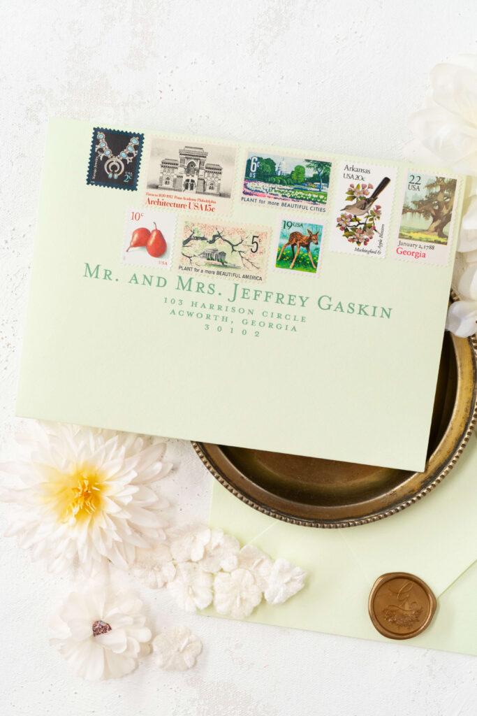 Wedding envelopes in beautiful light green have eight vintage stamps. E Stokes Creations curates a selection of vintage postage for clients based on their wedding aesthetic and the relationship between the clients. Pictured here includes nature stamps and Georgia vintage stamps among other aesthetically beautiful vintage stamps.