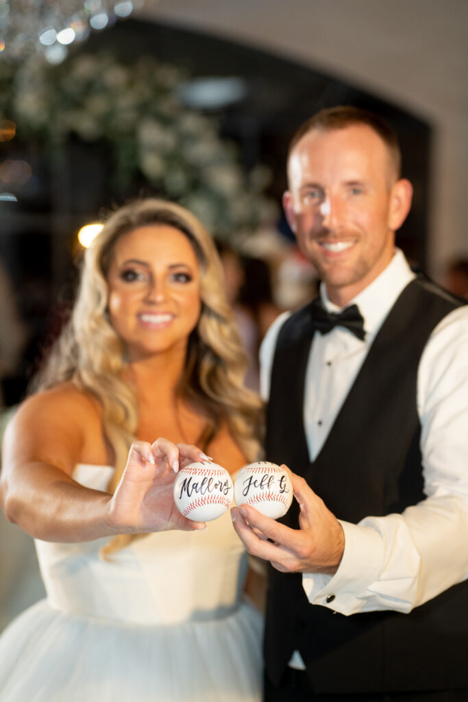 Mallory and Jeff pose with baseballs with their names, hand-lettered in calligraphy. After the wedding, the bride and groom and their guests were able to keep their baseballs as wedding keepsakes.