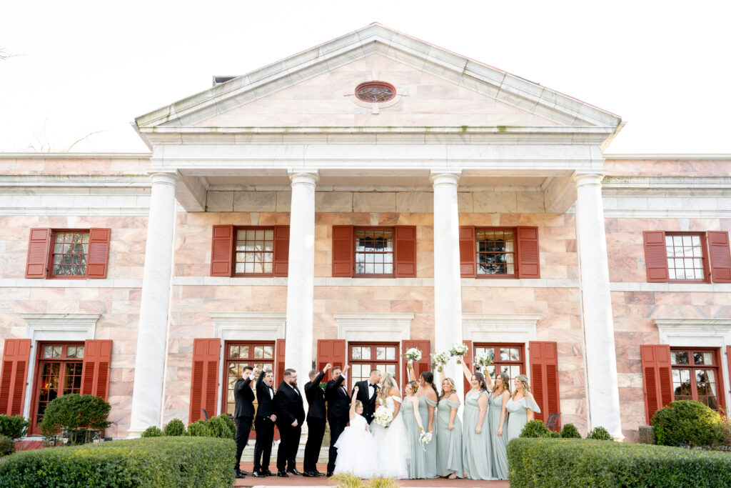 Bridal party outside of the front of the Tate House celebrating the Bride and Groom on their wedding day. The Tate House is a historic building with a salmon pink marble exterior.