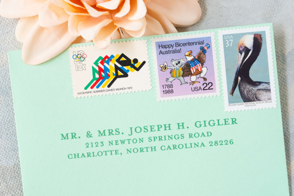 Close-up view of RSVP envelope showcasing vintage stamps featuring track runners, USA and Australian stamp and a pelican stamp.