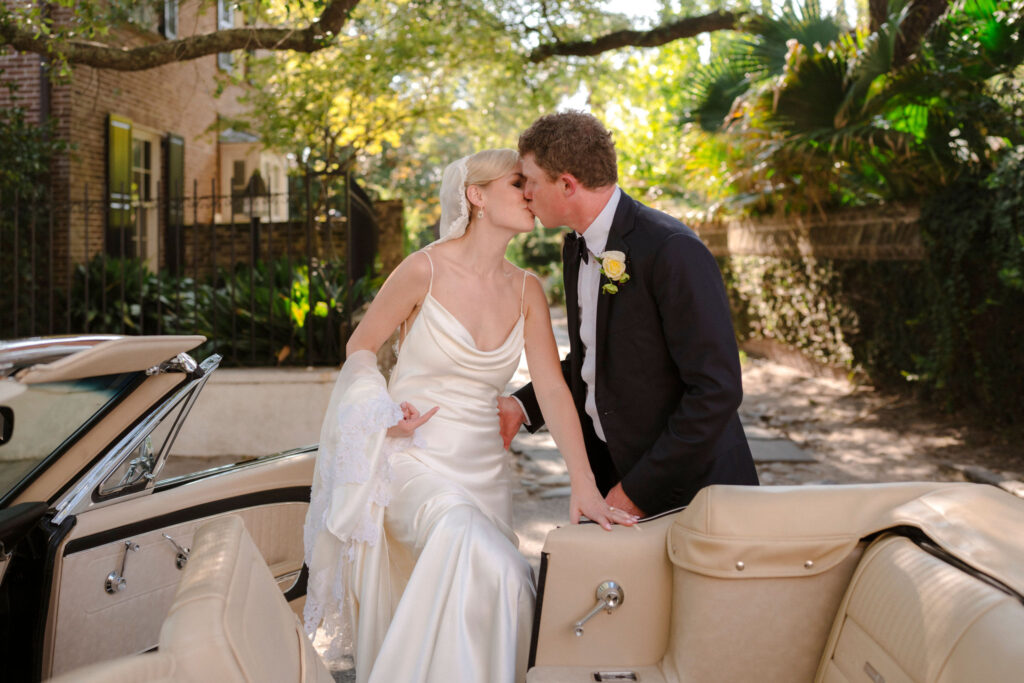 Bride and Groom share a kiss outside of the Gibbes Museum of Art on their wedding day while stepping into a classic car.